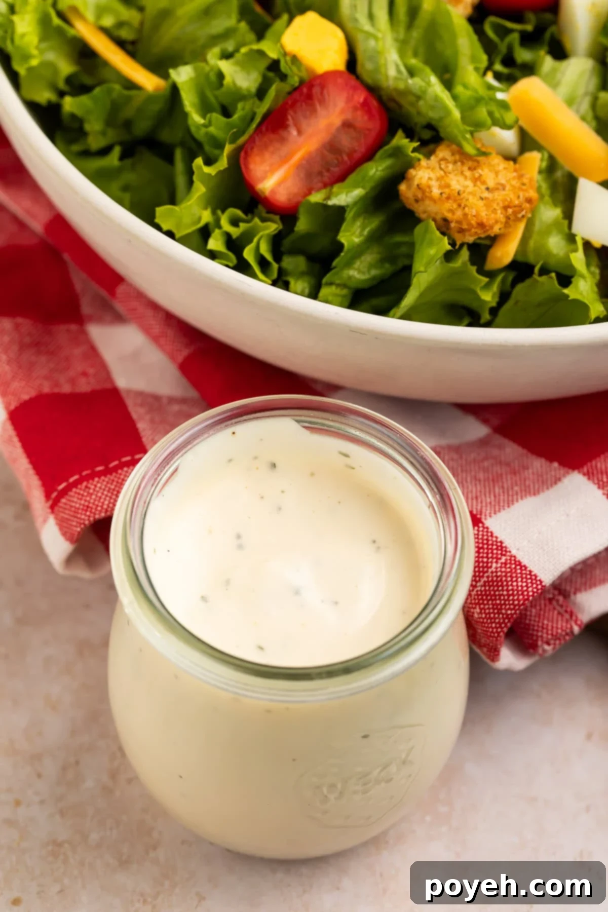 Glass jar of ranch dressing with a bowl of salad in the background.