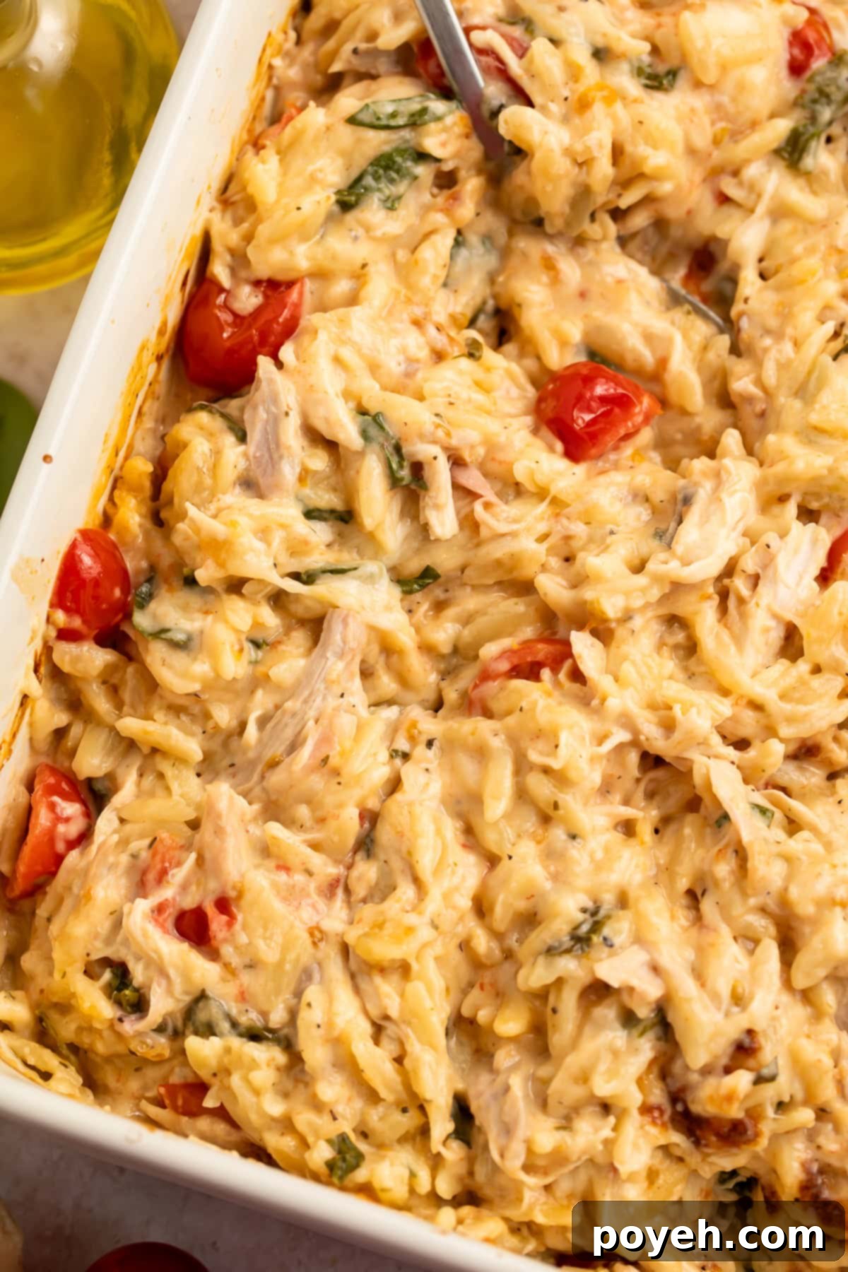 Close up of a stirred chicken and orzo bake in a white baking dish, showcasing its creamy texture and fresh ingredients.