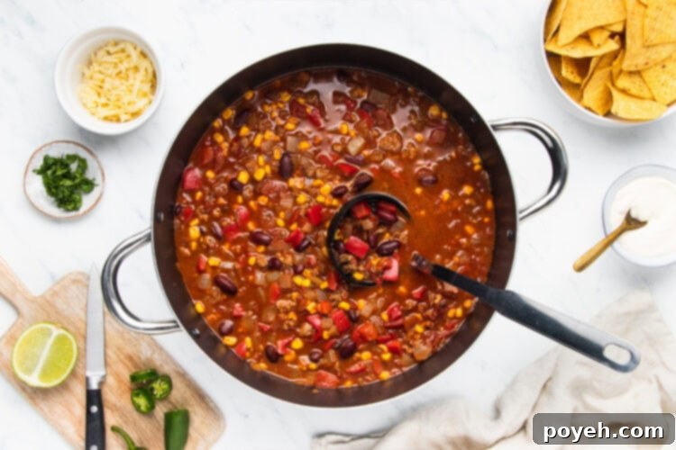 A ladle scooping hot, steamy chili with corn out of a large cooking pot, ready to be served.