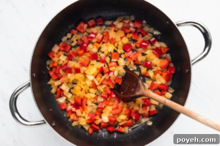 Onions and red bell peppers simmering in olive oil in a large pot, forming the base of the chili.