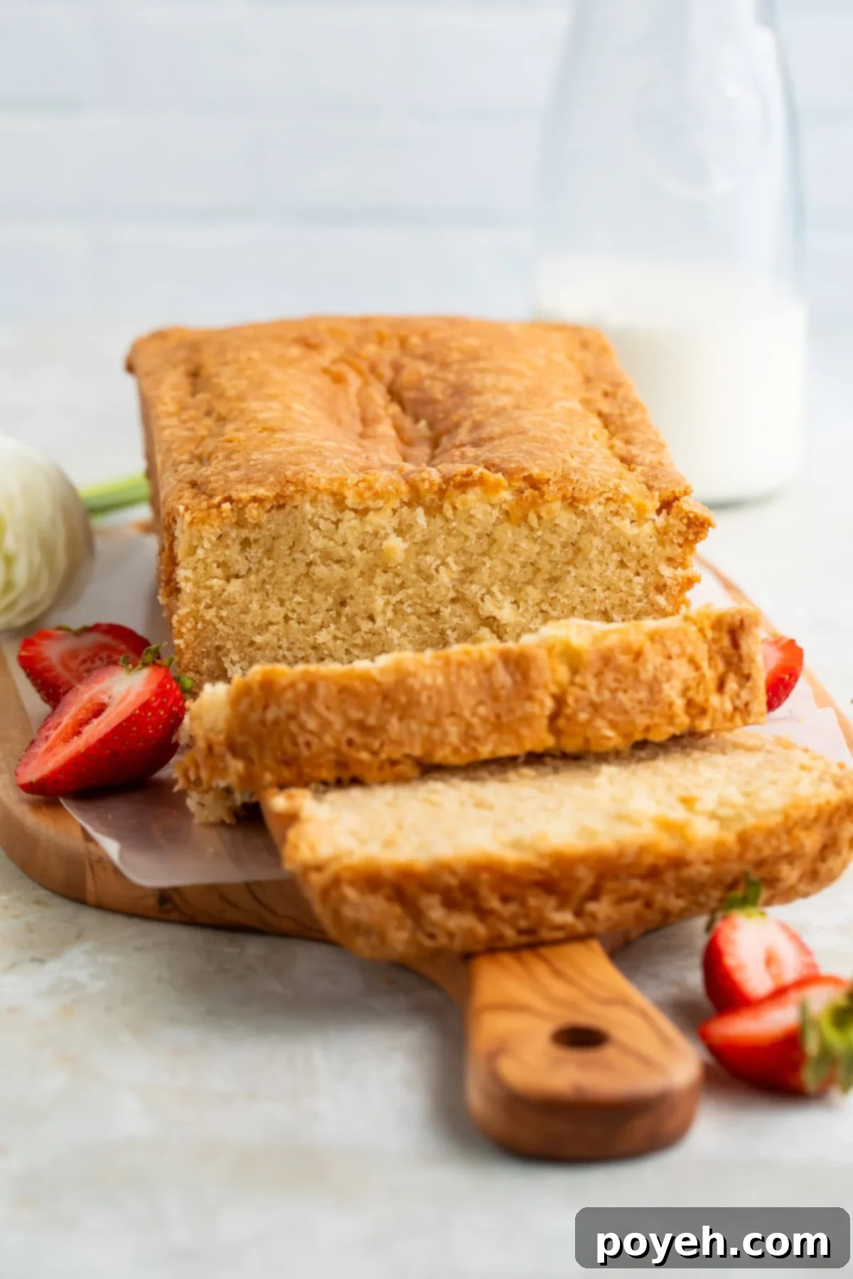 Sliced vegan pound cake on a wooden board with fresh flowers and sliced strawberries just visible off to the side.