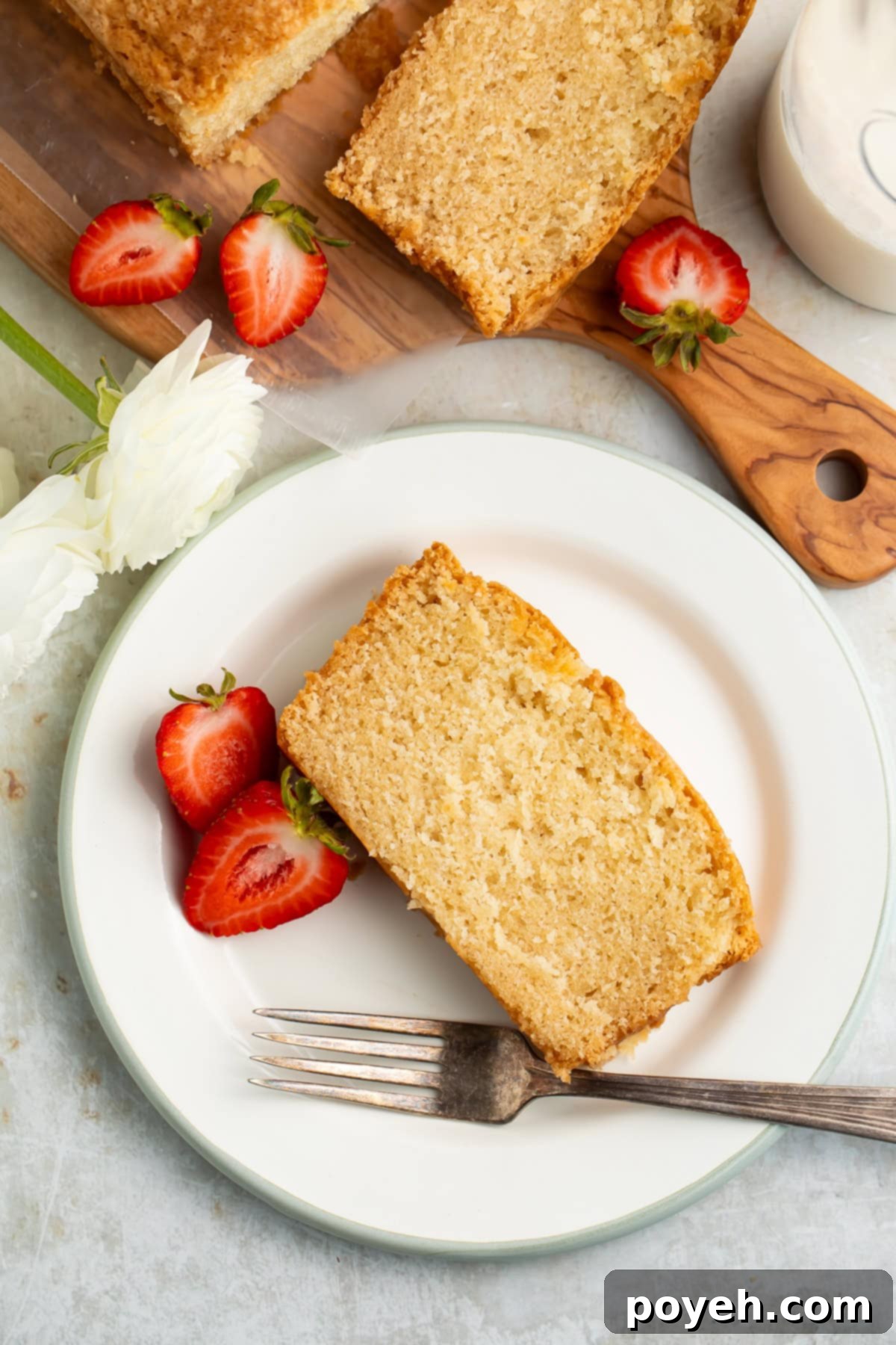 Slice of vegan pound cake on a white plate with a fork and a halved strawberry.