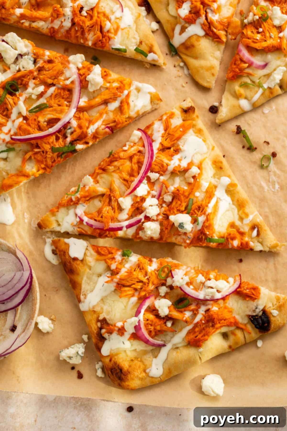 Triangles of flatbread topped with thinly sliced red onion, melted mozzarella cheese, shredded buffalo chicken, a drizzle of ranch dressing, and crumbled blue cheese for garnish.