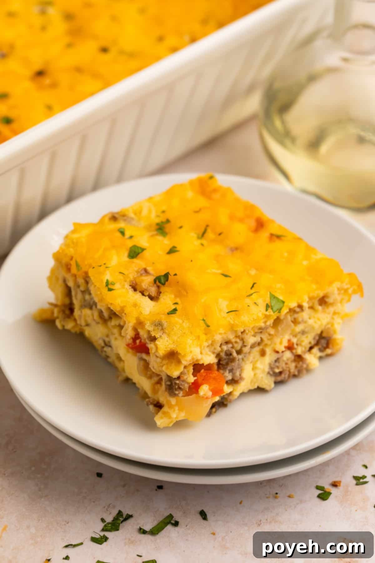 Slice of egg bake on a white plate with the casserole in the background in a white dish.