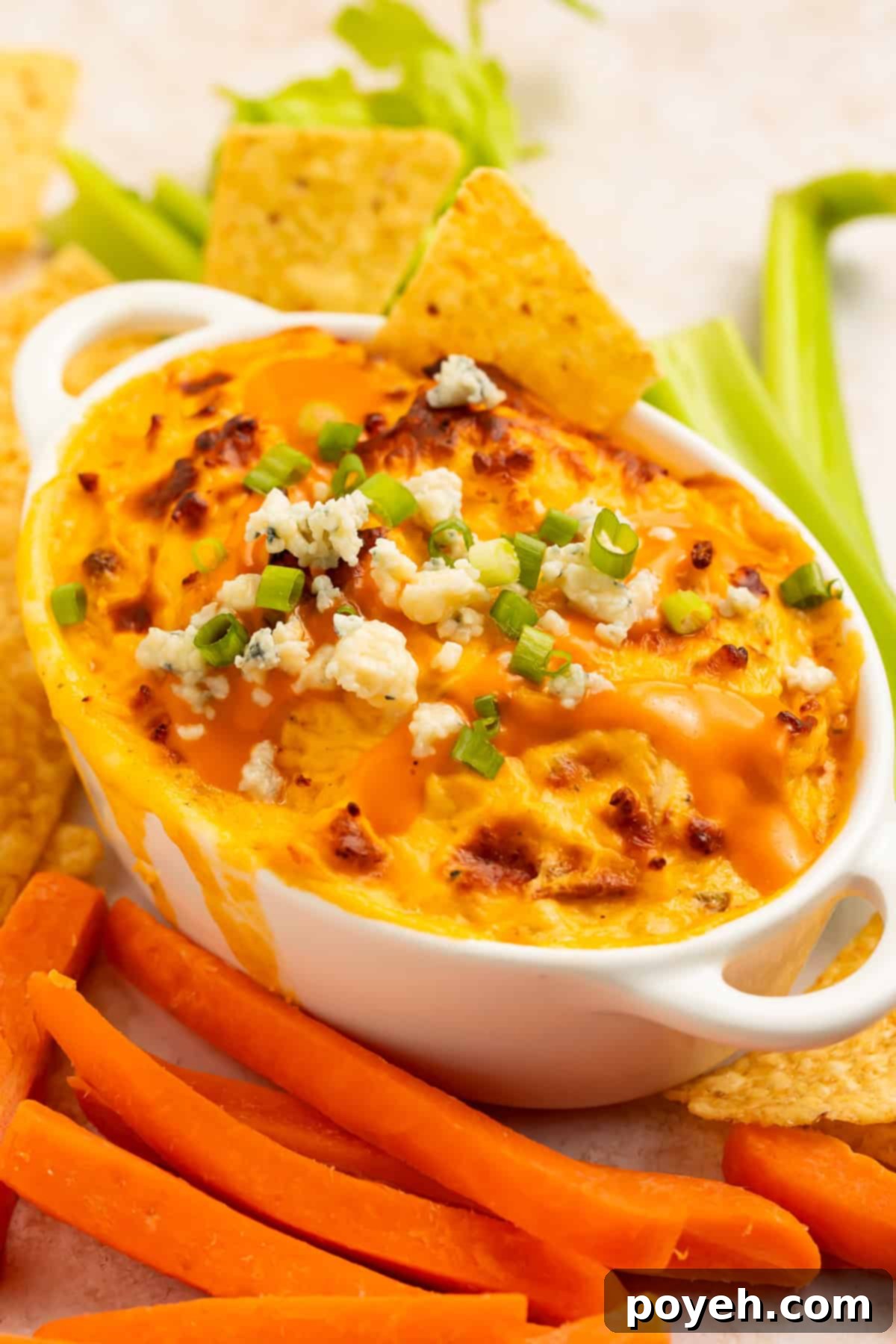 Creamy High Protein Buffalo Chicken Dip in an oval baking dish, garnished with crumbled cheese and sliced green onions.