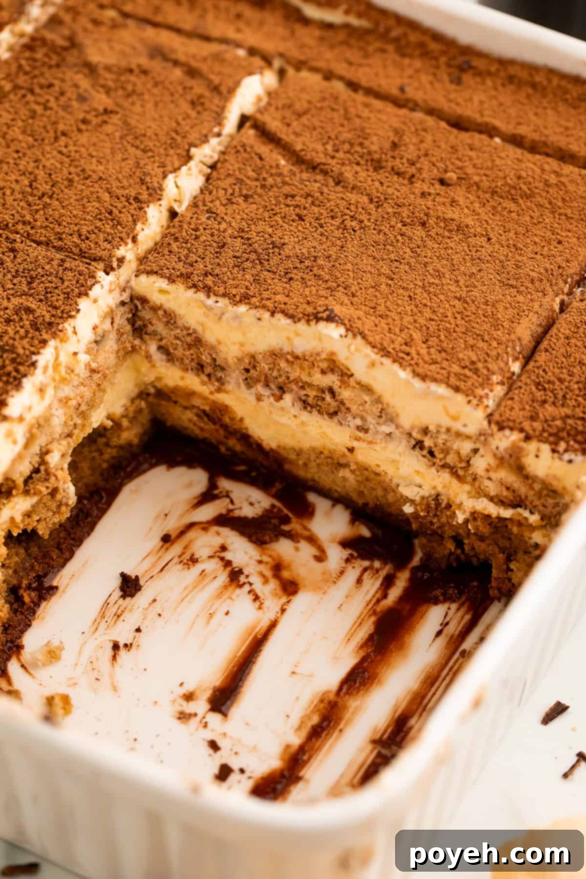 Side on view of slices of tiramisu in the pan with one missing to show the layers of the coffee chocolate dessert.