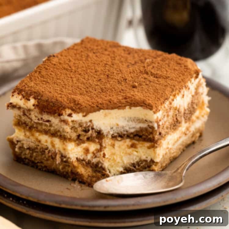 Slice of tiramisu on a plate with a spoon where a spoonful has just been taken out of the corner.