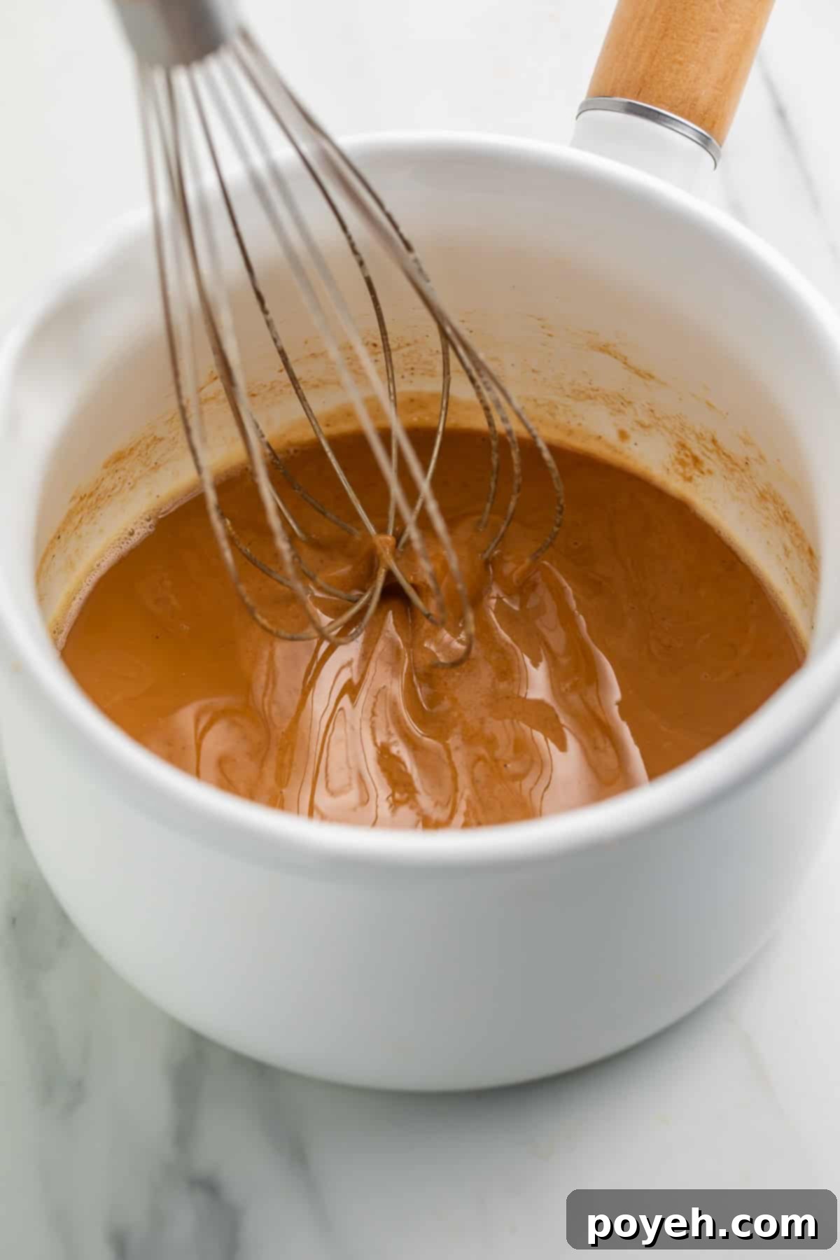 In progress gluten free roux being whisked in a white saucepan with a wooden handle. 