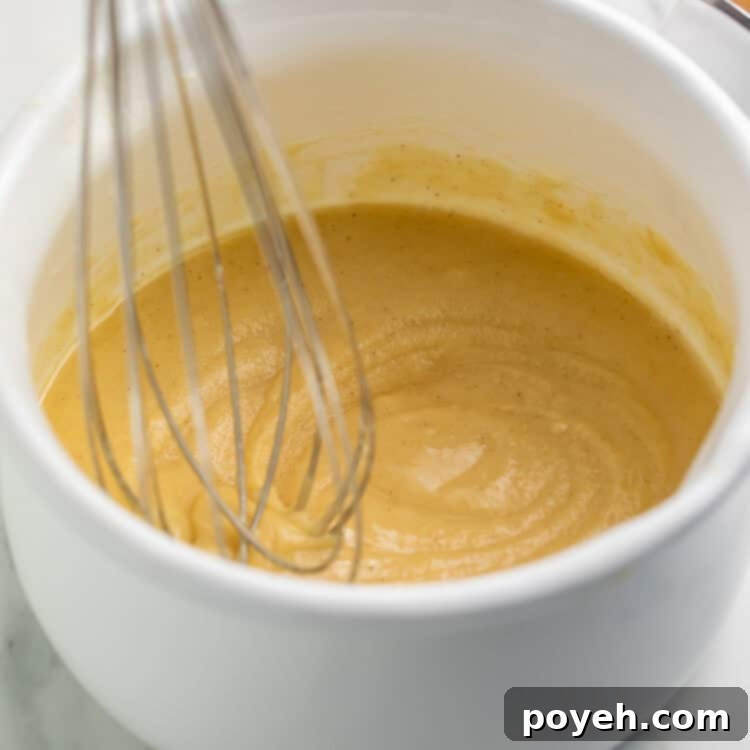 Whisk suspended against a finished white saucepan of gluten free roux.