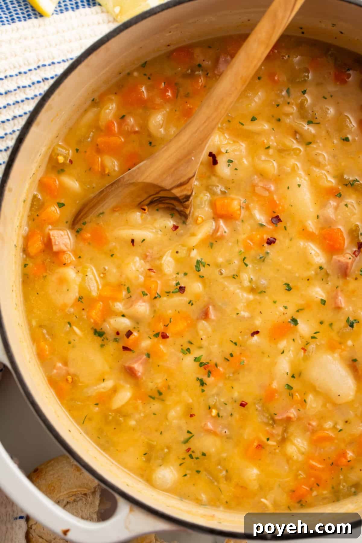 Wooden spoon being stirred in a white dutch oven of lima bean soup.