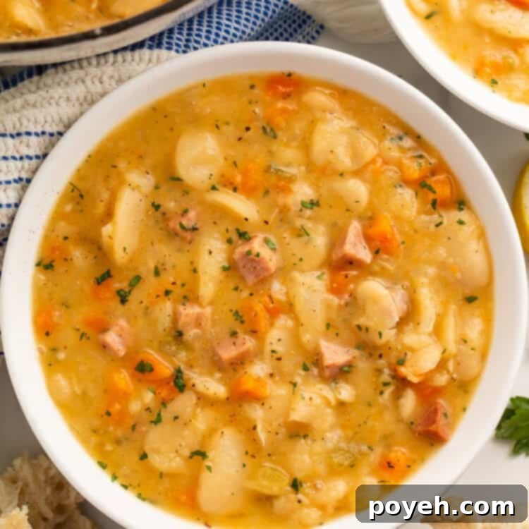 Close up of a white bowl of lima bean soup with another bowl and the casserole pot visible off to the side.