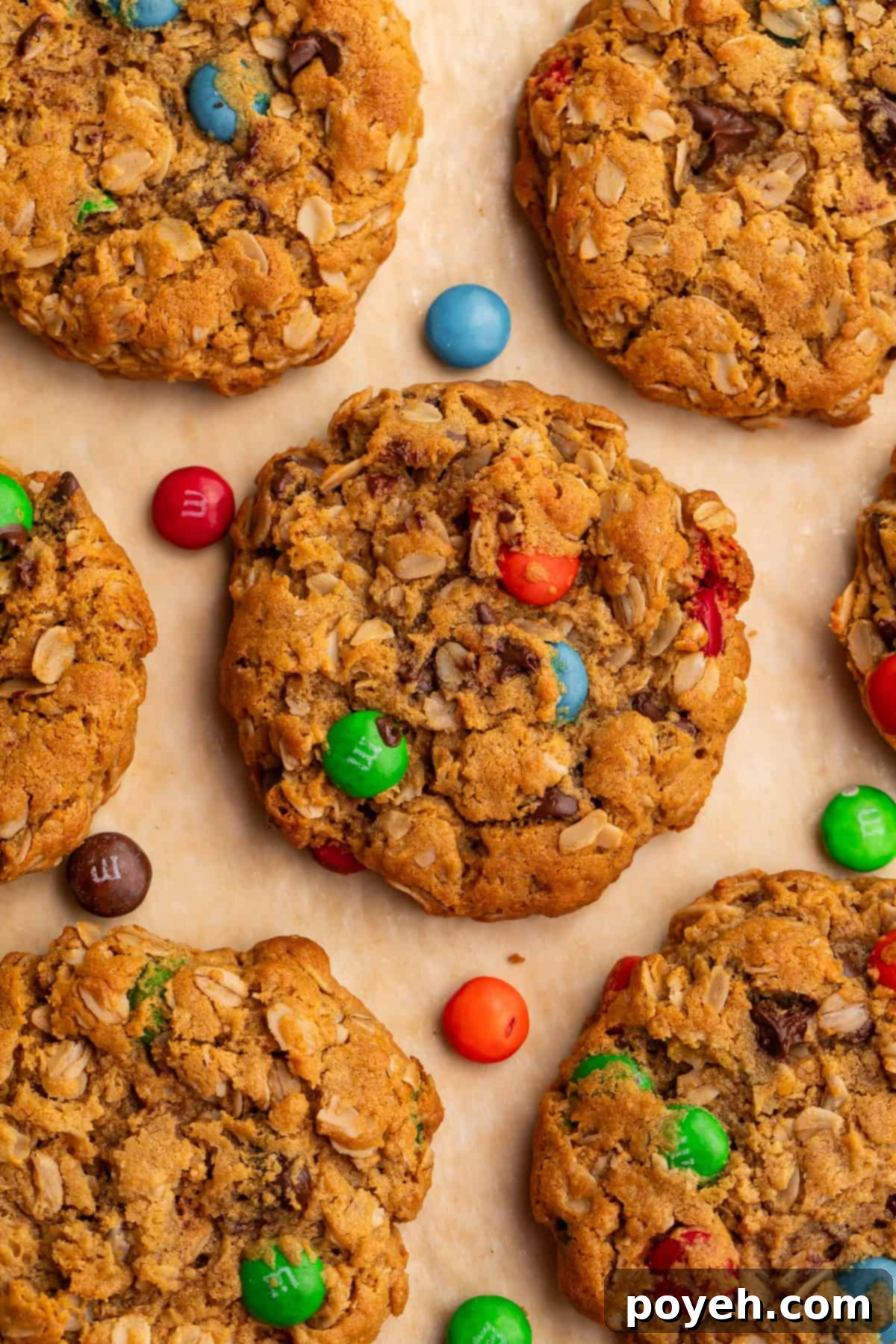 Close up of a batch of freshly baked monster cookies pictured overhead with colorful M&M candies scattered around them on a rustic wooden surface.