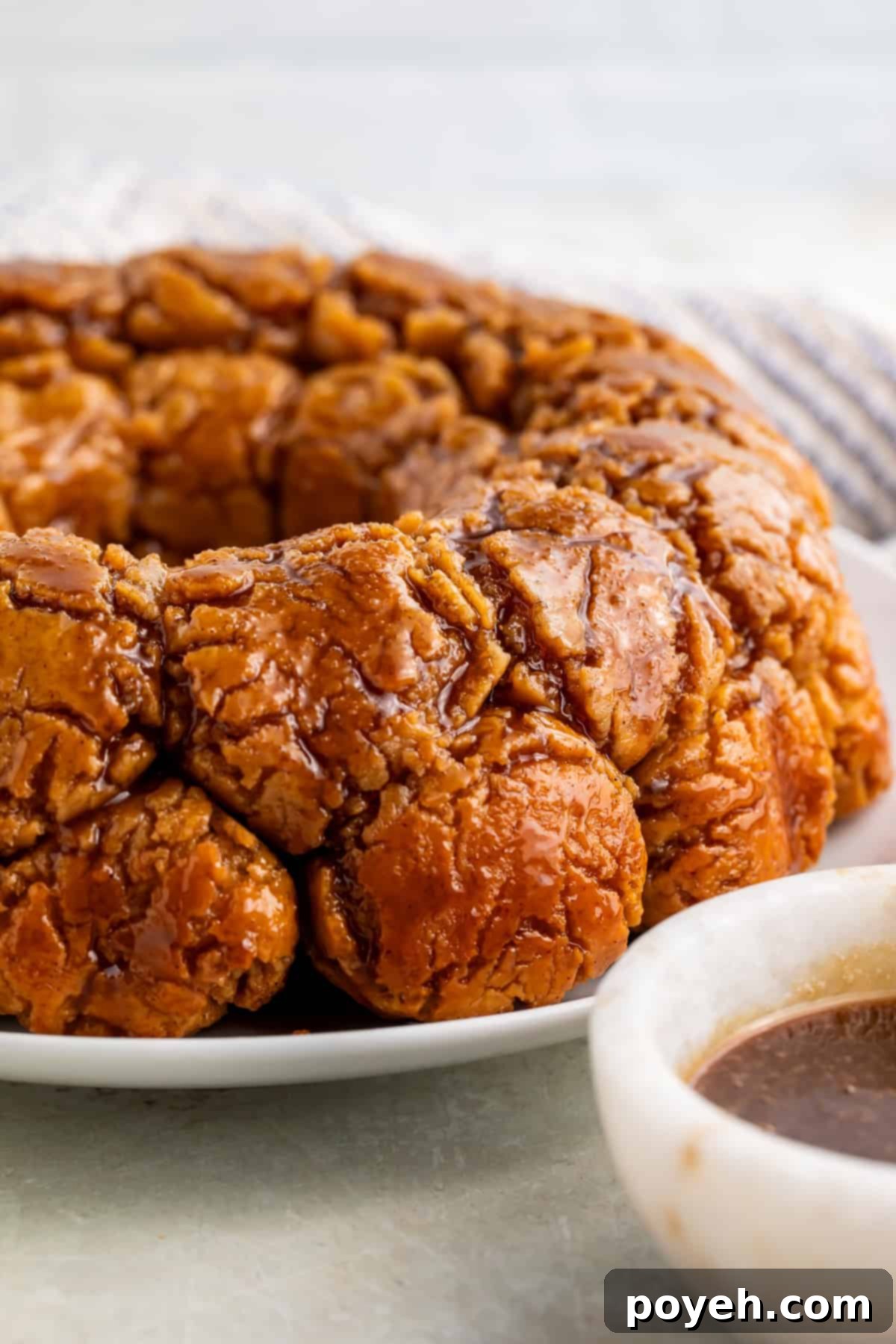 Gooey Gluten-Free Monkey Bread Bliss 2 Side on view of monkey bread on a white plate with a white bowl of caramel off to one side.