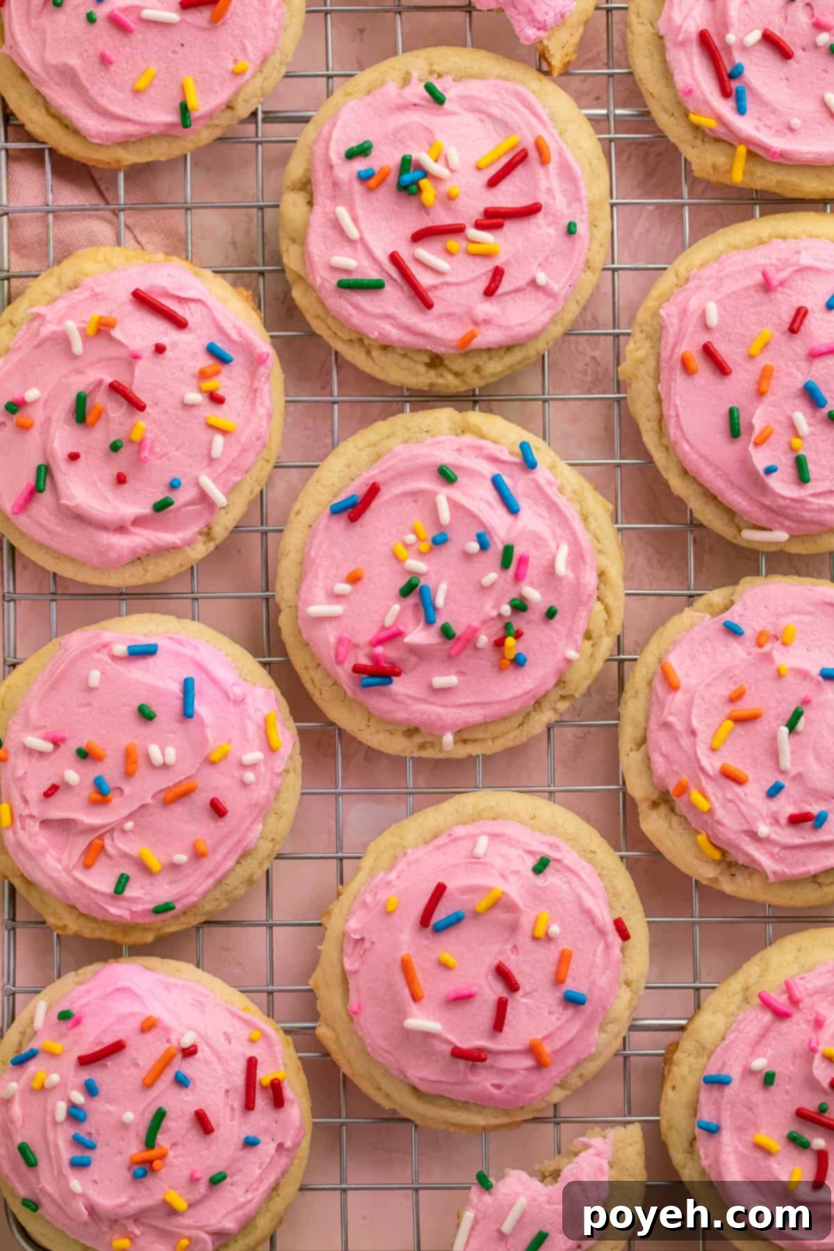 Pink frosted sugar cookies with rainbow sprinkles on a cooling rack, showcasing their perfect shape.