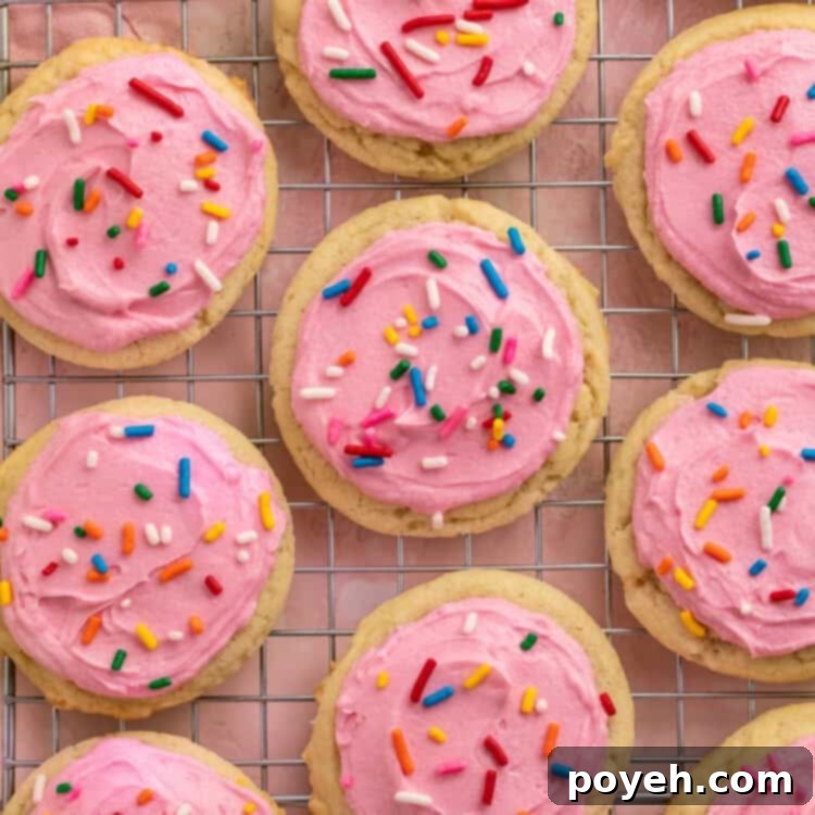 Pink frosted sugar cookies with rainbow sprinkles on a cooling rack.