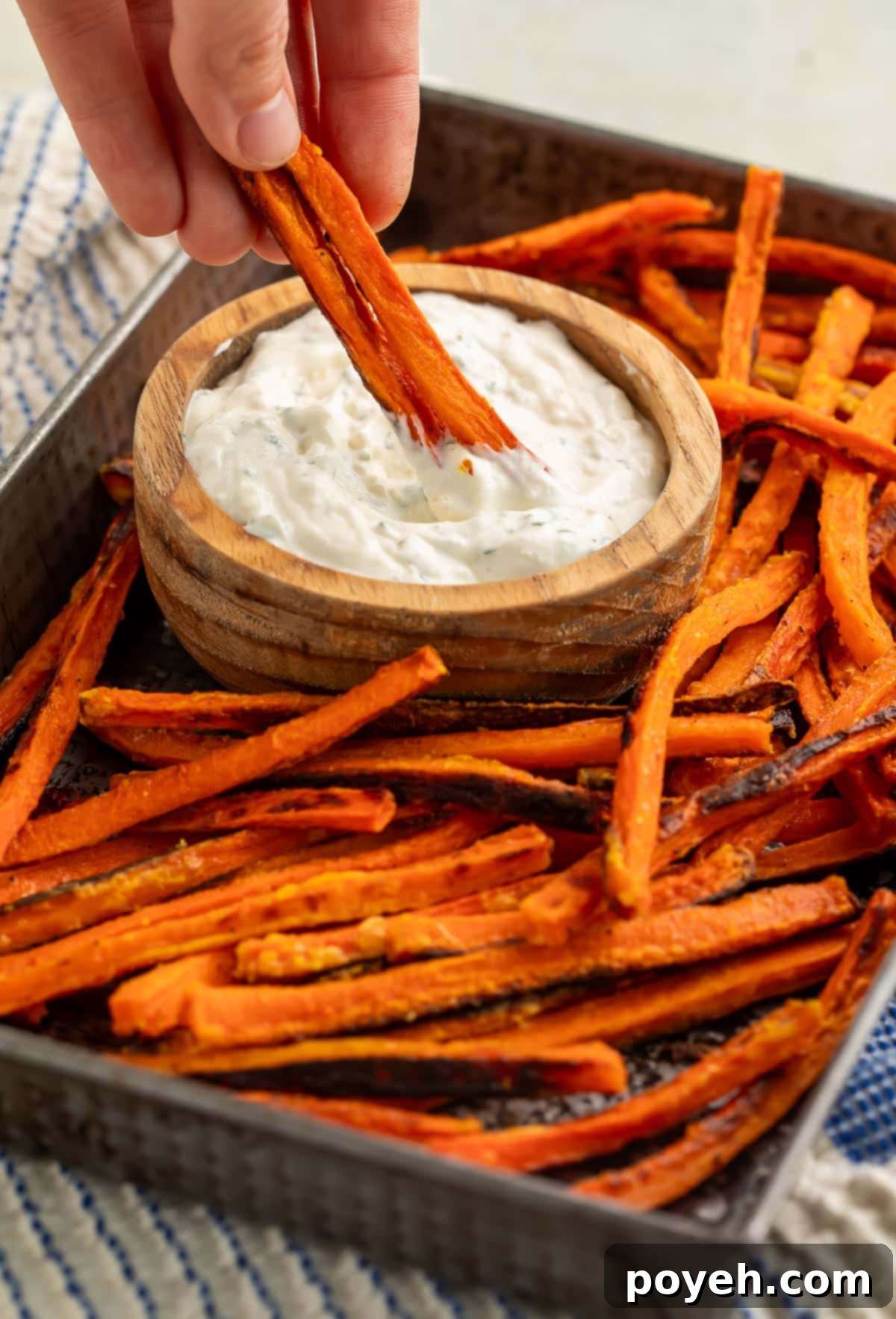 Golden brown carrot fries being dipped into a small wooden bowl of creamy, fresh herb dip. The fries are perfectly roasted, showcasing their natural sweetness and savory seasoning.