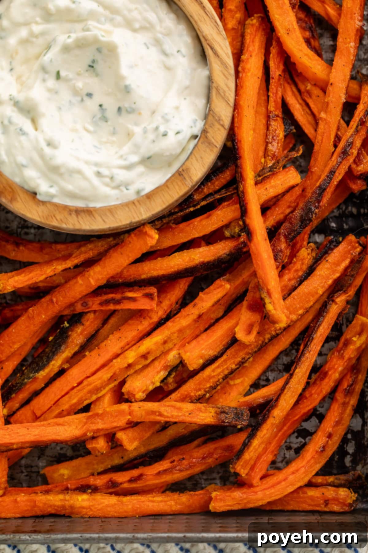 Close up shot of a baking tray filled with perfectly golden, oven-baked carrot fries, with a small bowl of creamy dip in the upper left corner.
