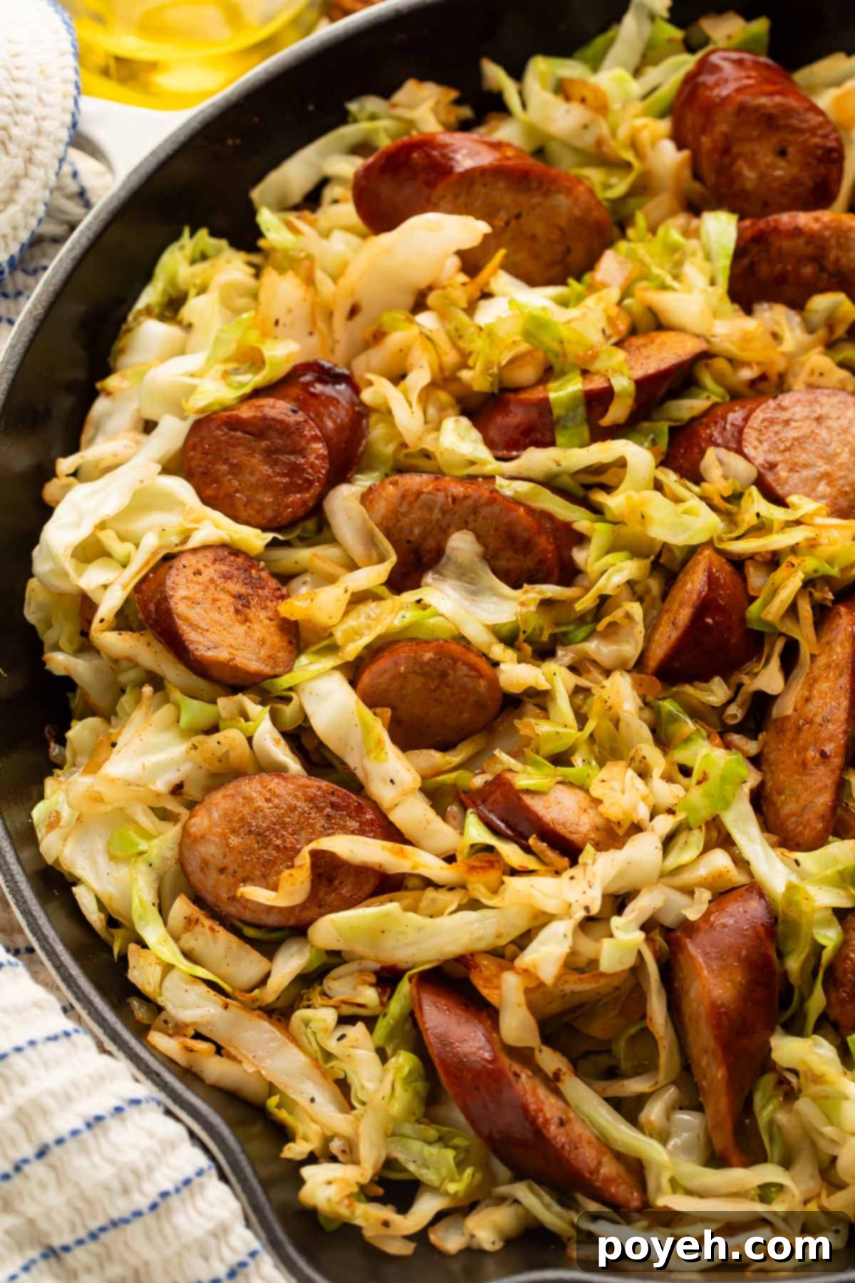 Close-up of cooked kielbasa and cabbage with a wooden spoon.