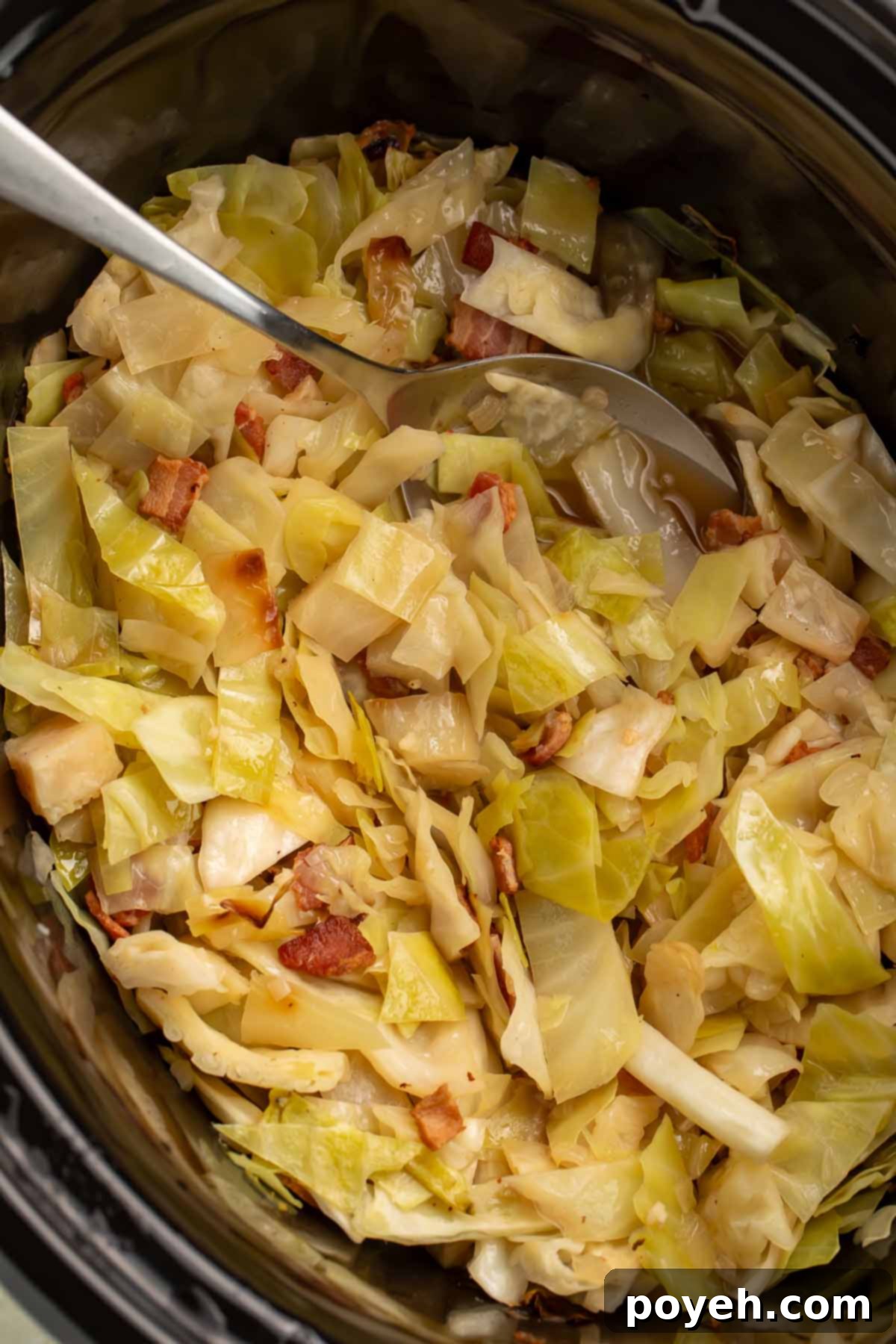 A close-up of tender Crockpot cabbage with crispy bacon bits, served in a slow cooker with a large silver spoon, ready to be enjoyed.