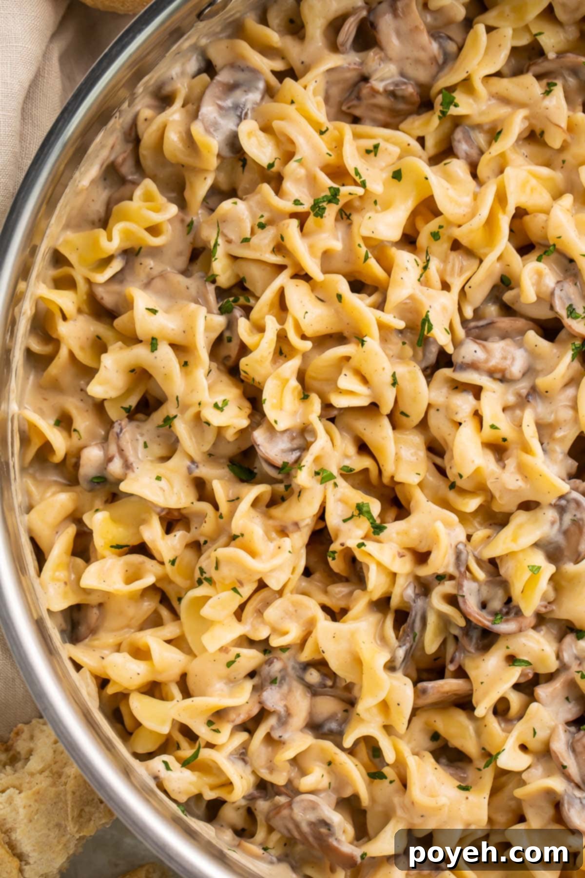 A large stainless skillet holding mushroom stroganoff made with egg noodles and pieces of baby bella mushrooms.