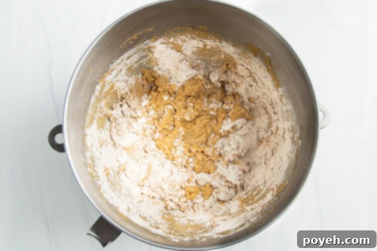 Overhead view of a silver stand mixer bowl with gluten-free flour being gradually added to the creamed butter and sugar mixture.