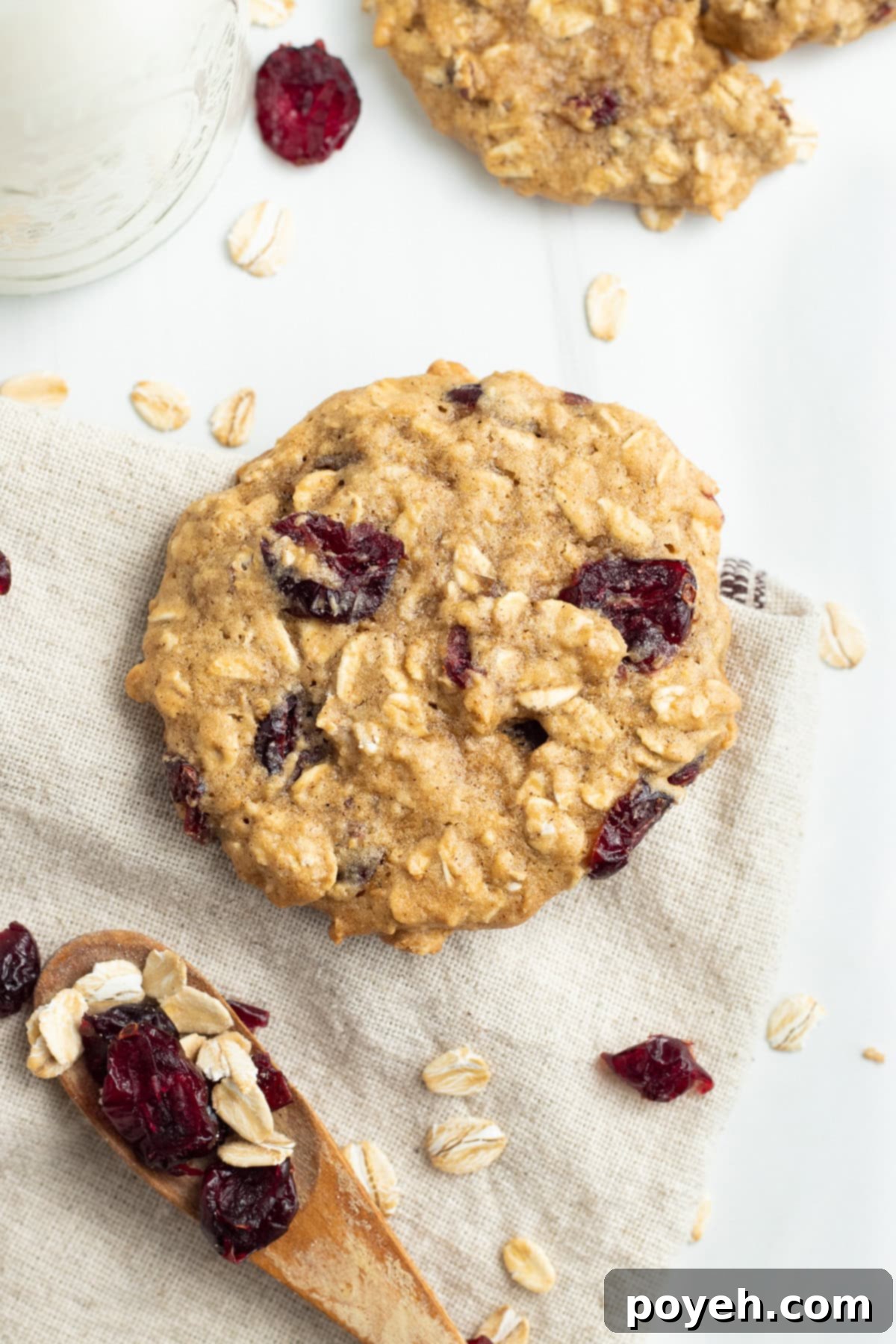 A single perfectly baked cranberry oatmeal cookie resting on a napkin, with a wooden spoon featuring cranberries and oats nearby, highlighting the key ingredients.