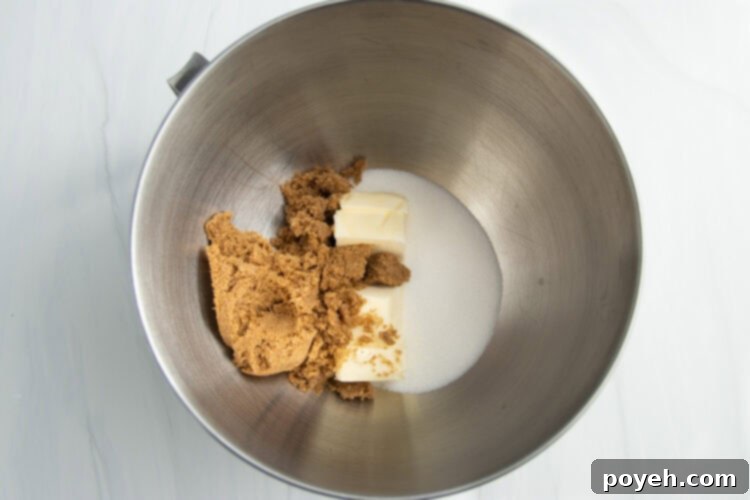 Overhead view of creamed butter, brown sugar, and white sugar in a large metal mixing bowl from a stand mixer.