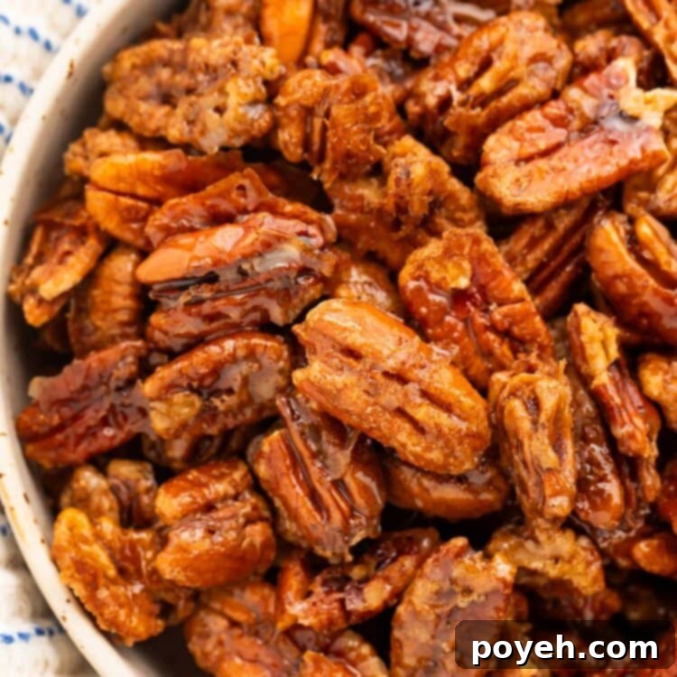 A bowl of maple-cinnamon glazed pecans sits on a table surrounded by a white and blue striped kitchen towel.