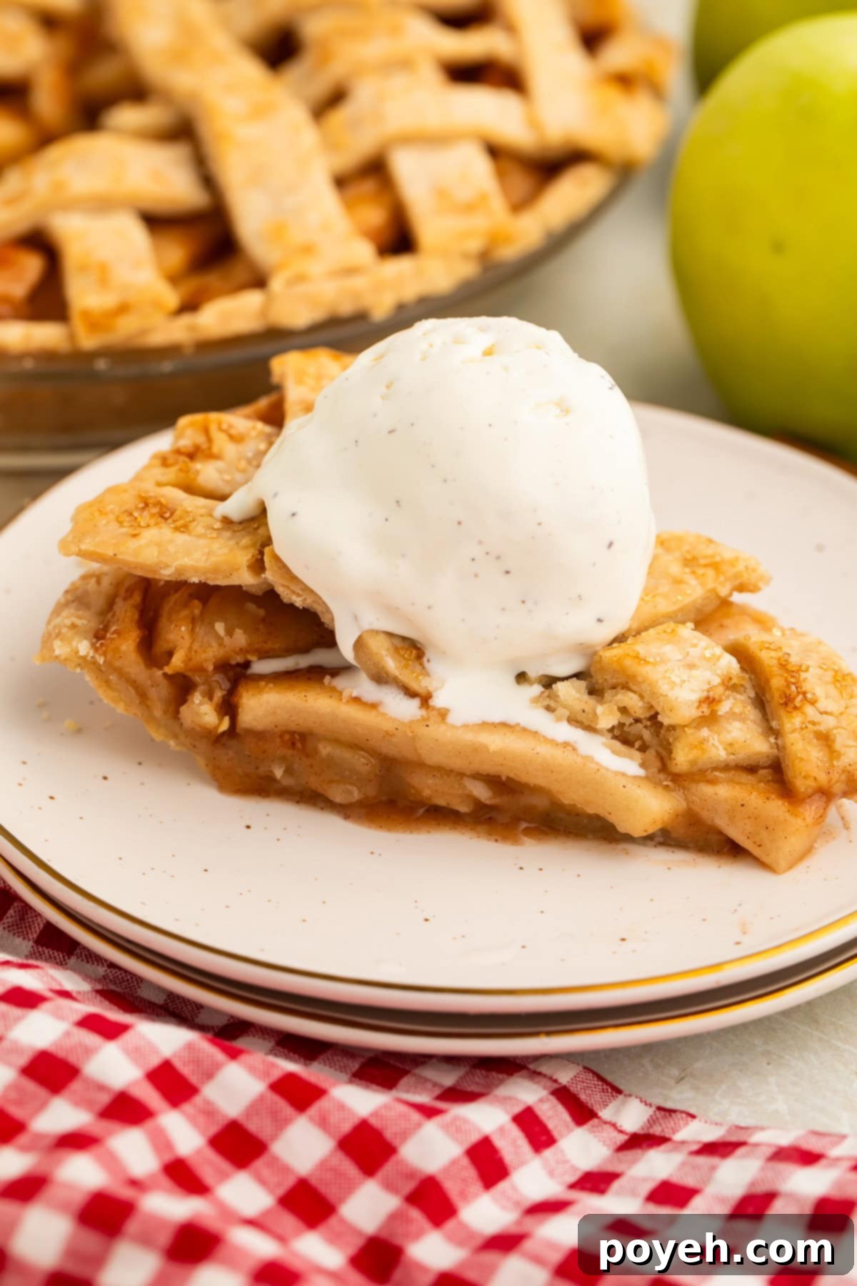 A perfectly baked slice of warm, crisp vegan apple pie, glistening with spiced apple filling, topped with a generous scoop of creamy vanilla bean vegan ice cream, elegantly resting on a white plate, ready to be enjoyed.