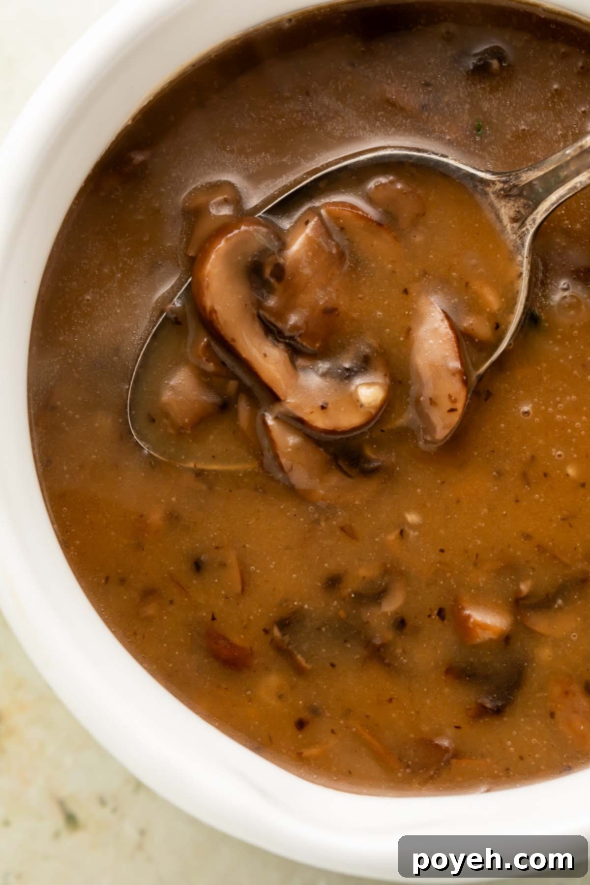 A spoonful of tender, perfectly cooked mushrooms being lifted out of a creamy white bowl of homemade vegan mushroom gravy, showcasing its rich texture and enticing color.
