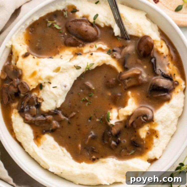 A large bowl of fluffy mashed potatoes topped generously with rich, dark vegan mushroom gravy, ready to be served.
