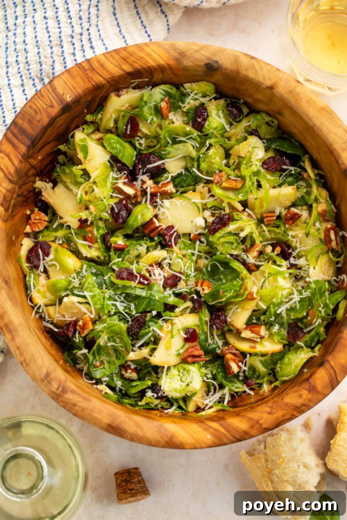 A beautifully presented wooden bowl filled with a fresh shredded Brussels sprouts salad, featuring crisp apple slices and vibrant dried cranberries.