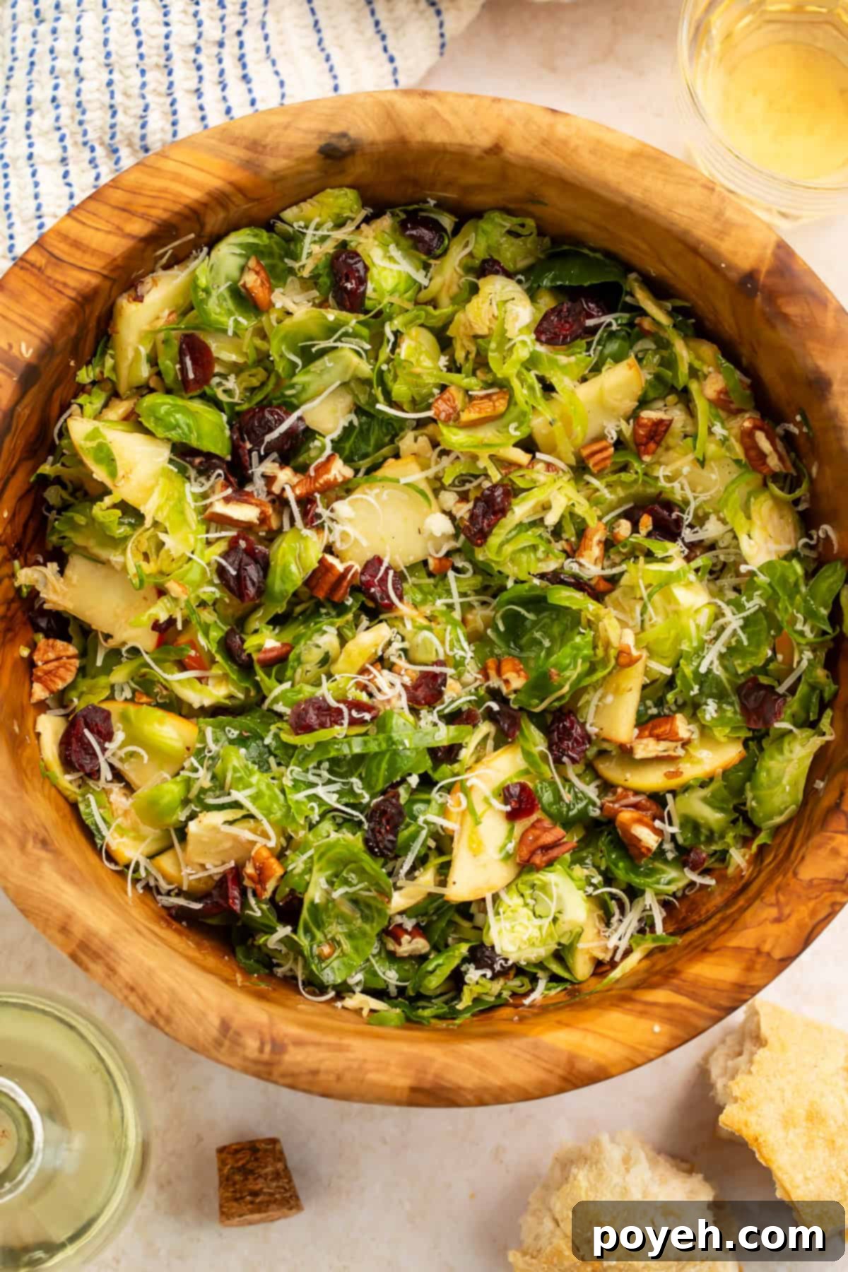 A close-up view of the vibrant shredded Brussels sprouts salad, highlighting the texture of the sprouts, apple slices, and dried cranberries in a rustic wooden bowl.