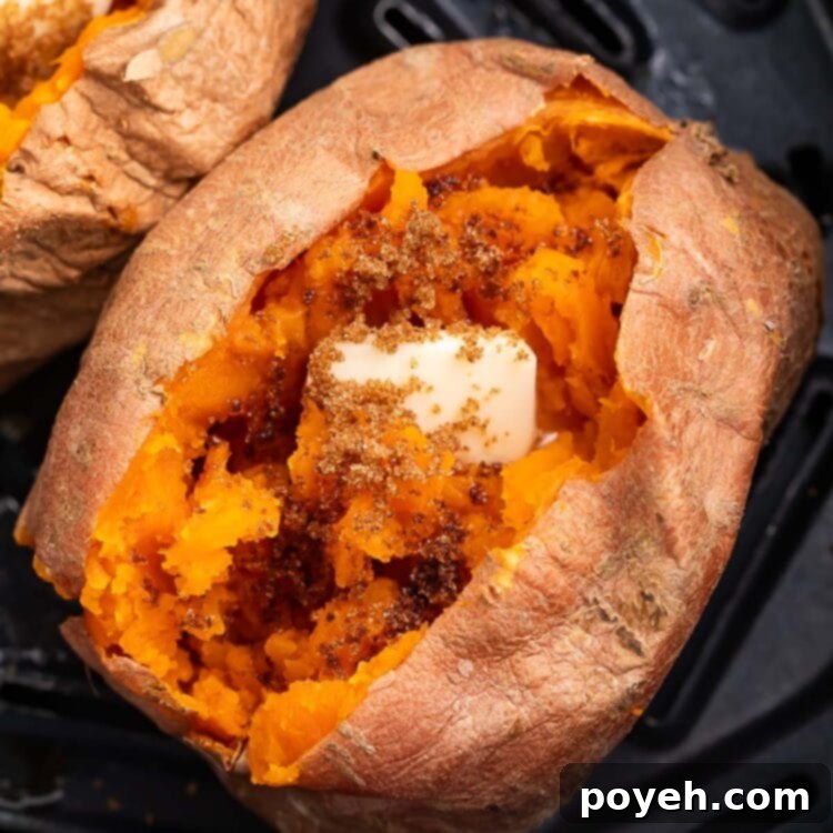 A cooked sweet potato resting in an air fryer basket. The top of the potato is split open, with the insides fluffed and topped with a pat of butter.