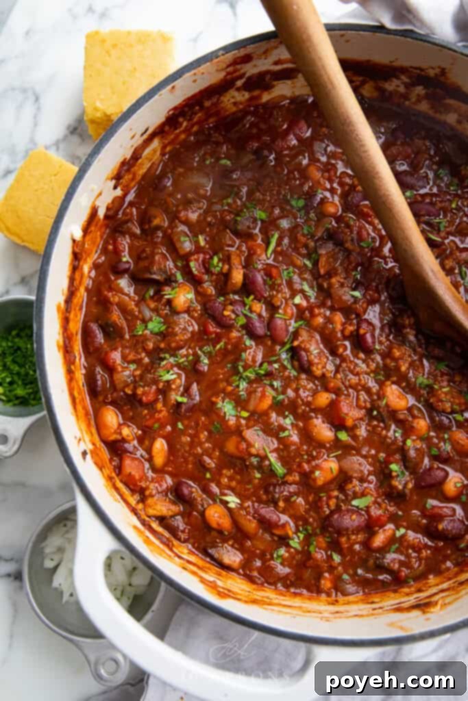 An inviting overhead shot of a hearty bowl of vegan chili, rich with tomatoes, various beans, and quinoa, garnished with fresh cilantro.