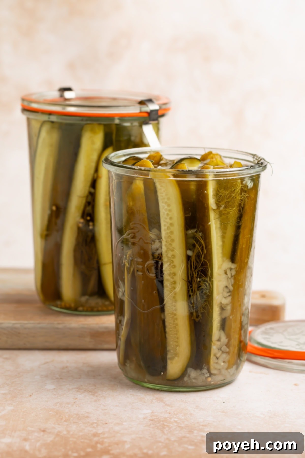 Two jars of homemade dill pickles, the lid removed in the jar in the front of the picture.