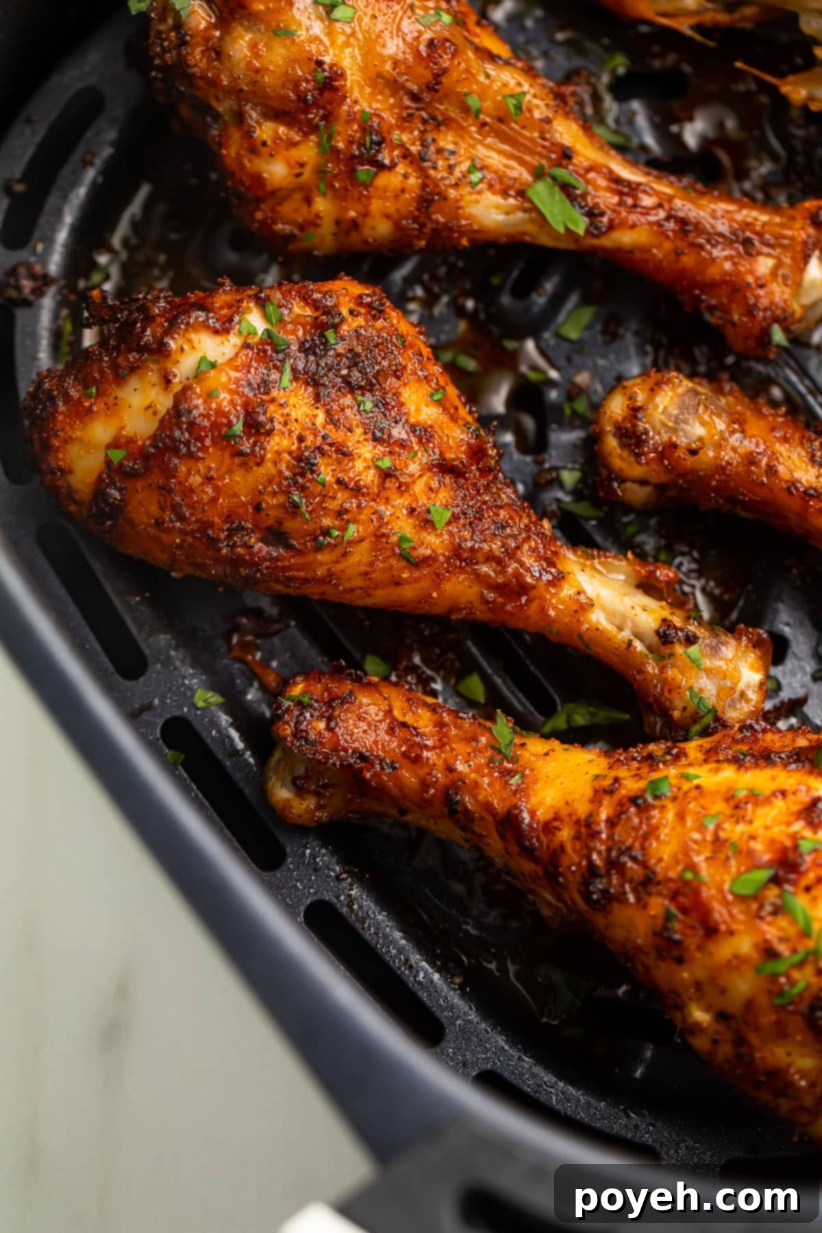 Close-up of perfectly crispy air fryer chicken legs, golden brown and seasoned, resting in a black air fryer basket.