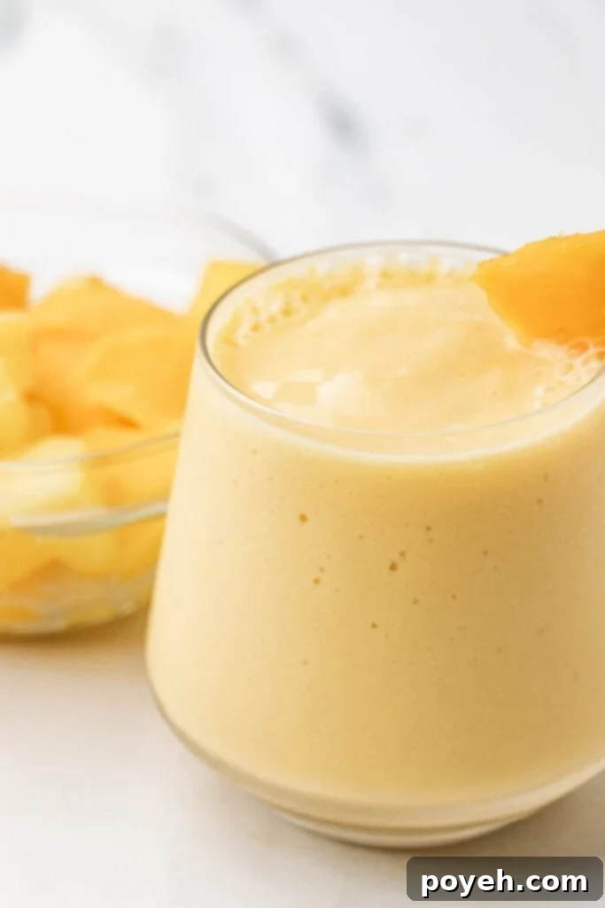 Delicious and creamy mango pineapple smoothie in a tall glass, garnished with fresh fruit.