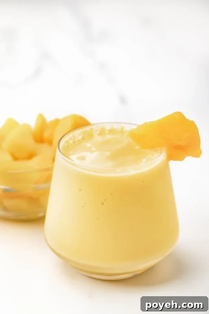 Mango pineapple smoothie in a clear glass with a straw, ready to be enjoyed.