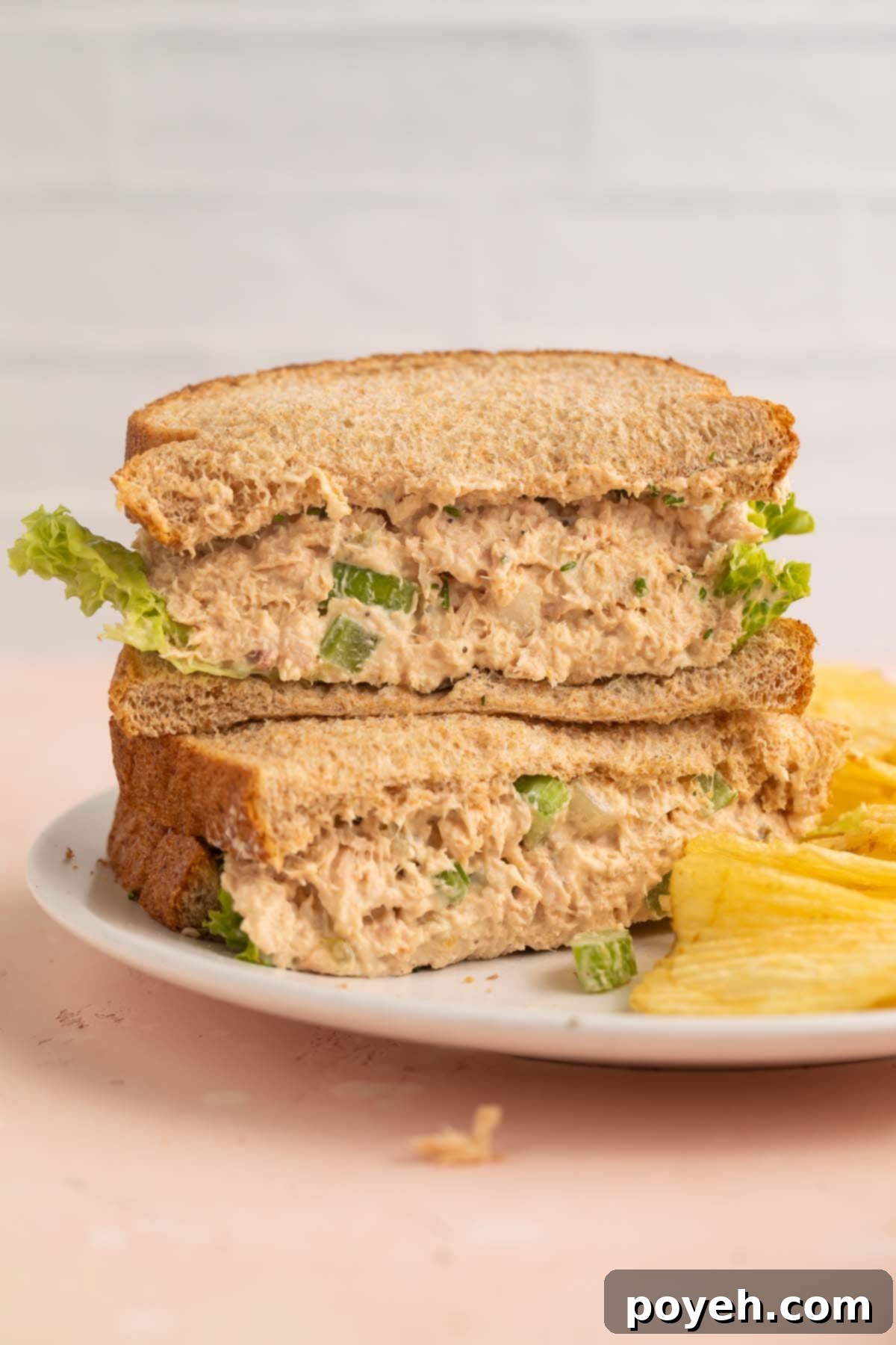 A tuna salad sandwich, halves stacked on top of each other on a plate with potato chips.