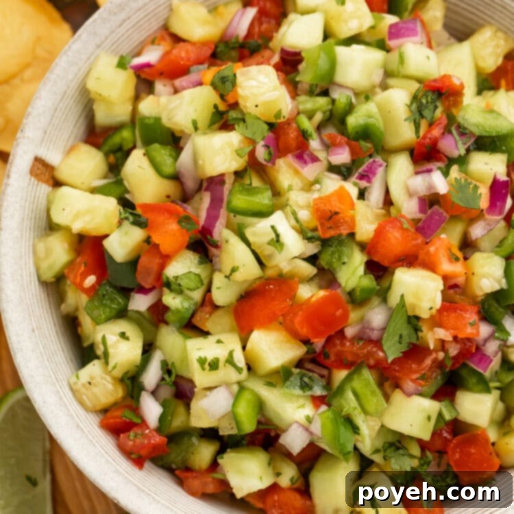 Close-up overhead shot of cucumber salsa with tomato and onion in a large bowl.