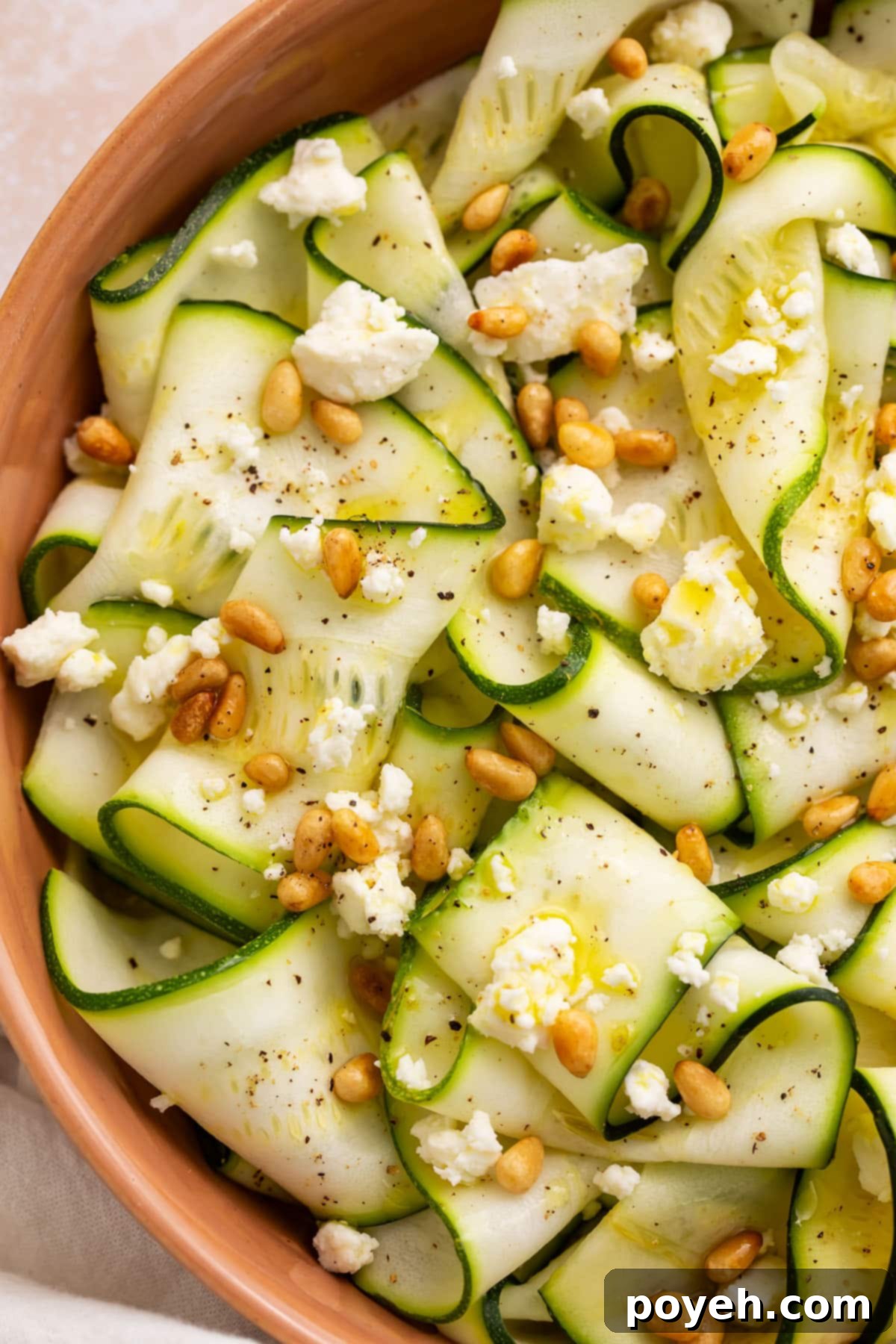 Close-up of zucchini salad in a terra cotta bowl. The salad has strips of zucchini, toasted pine nuts, and crumbled cheese.