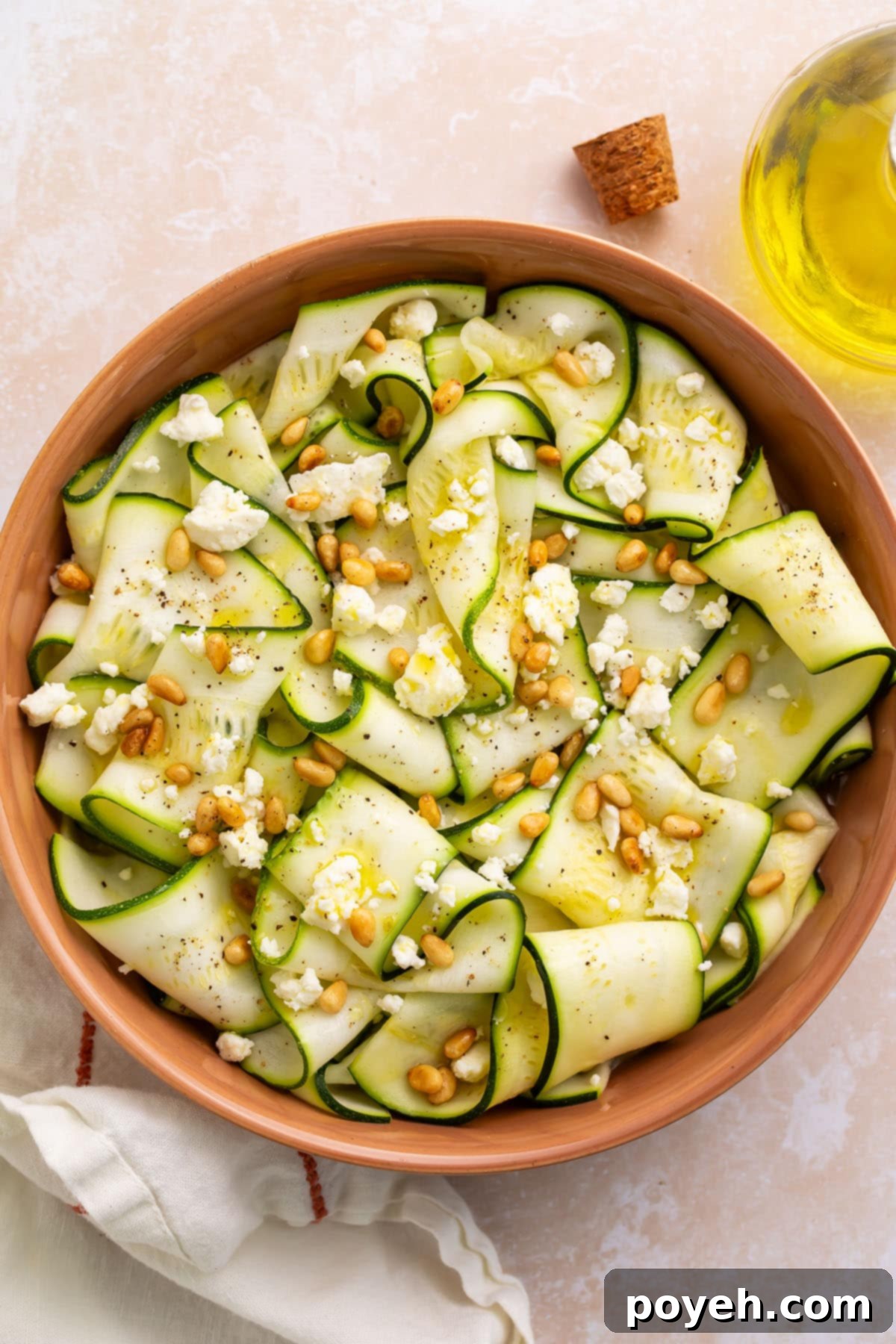 Zoomed out, overhead photo of a bowl of zucchini salad with pine nuts and cheese crumbles.