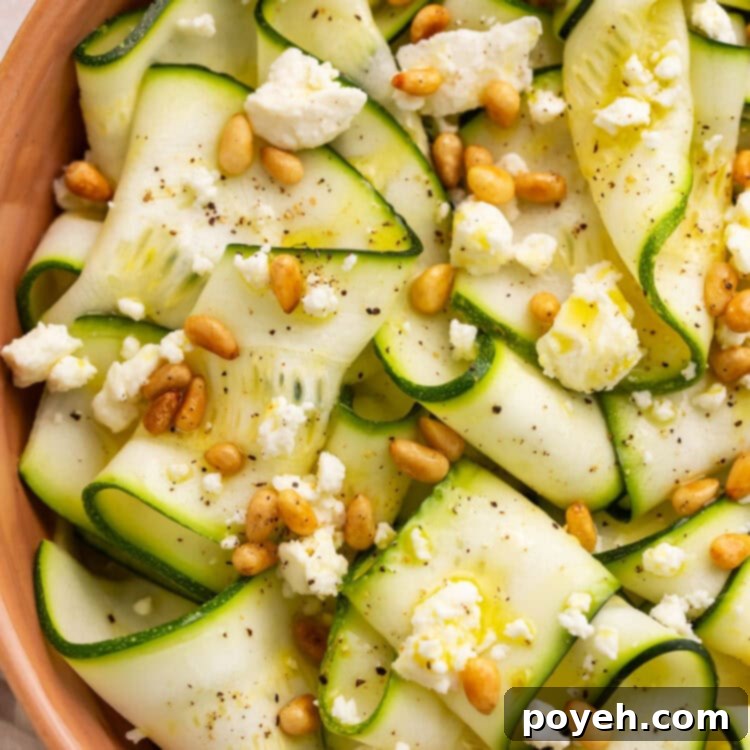 Close-up of zucchini salad in a terra cotta bowl. The salad has strips of zucchini, toasted pine nuts, and crumbled cheese.