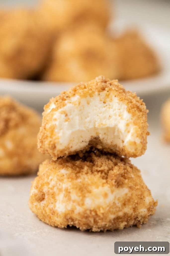 Stacked cheesecake cream cheese fat bombs, with a bite taken out of the top one, showcasing their creamy texture and delicious crumble coating.