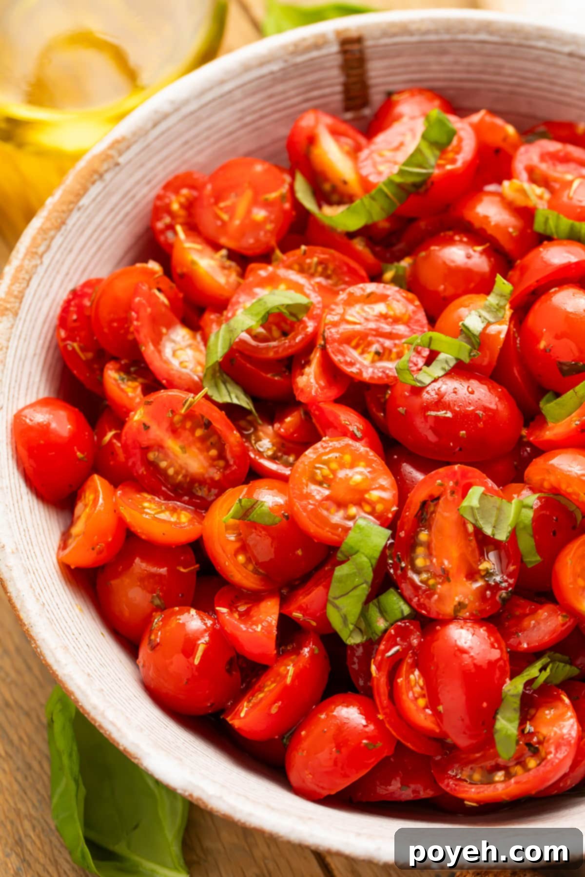 Top-down view of a bowl of rich, bright red tomatoes with fresh green basil in a white bowl.