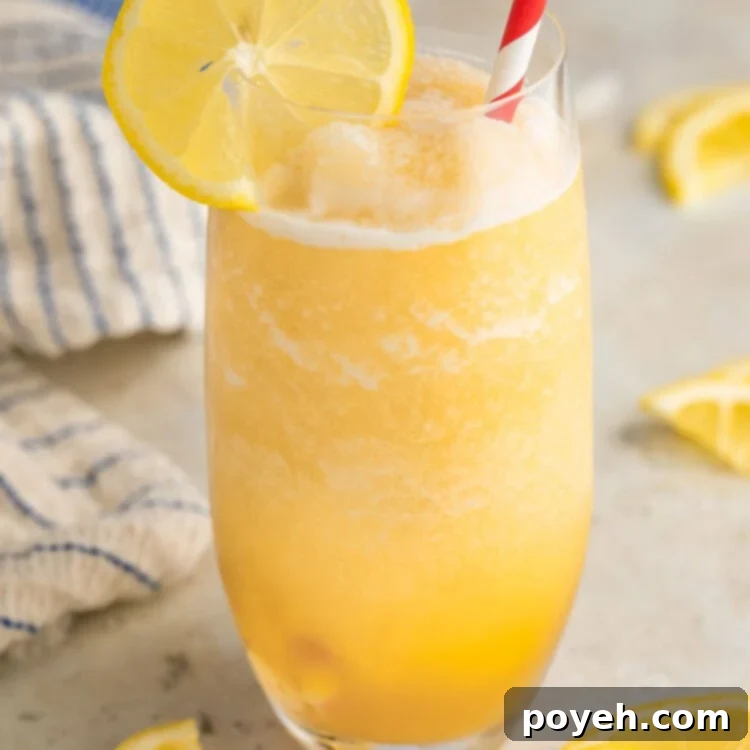 A tall glass filled with yellow frozen lemonade and garnished with a lemon coin and a red & white striped straw.