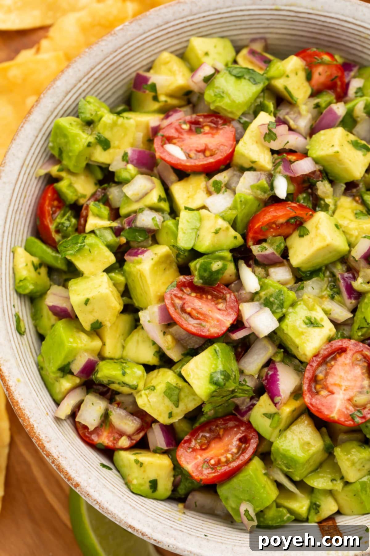 Zesty Chunky Avocado Tomato Salad 2 Close-up view of chunky guacamole salad with avocado and cherry tomatoes in a large white bowl, garnished with fresh cilantro.