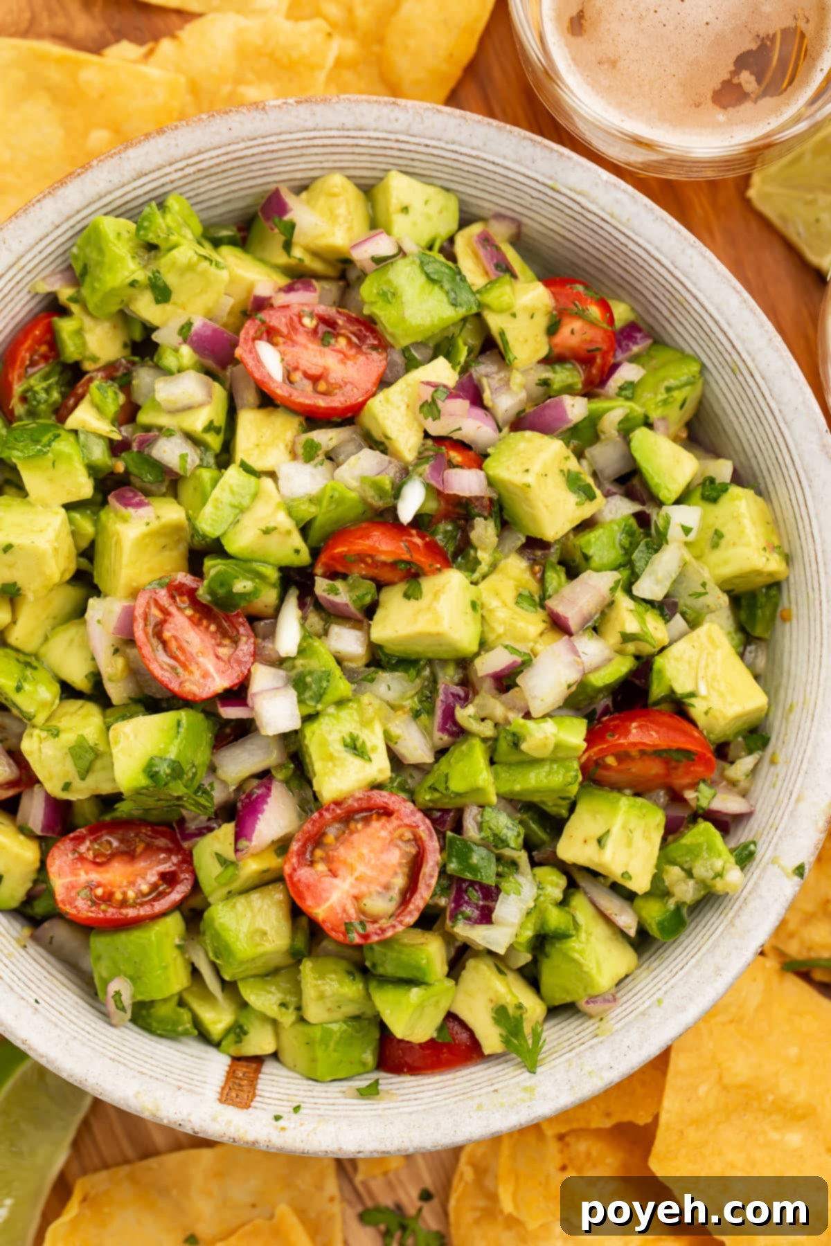 Zesty Chunky Avocado Tomato Salad 3 Close-up view of a large white bowl filled with chunky guacamole salad, featuring diced avocado, halved cherry tomatoes, and red onion.