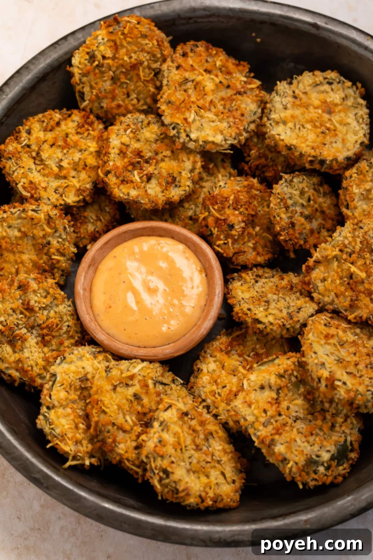 Black bowl of air fryer fried pickles with a small wooden bowl of creamy, spicy dipping sauce. 